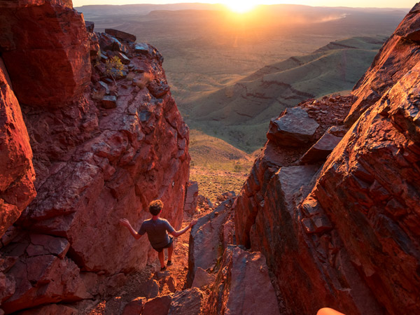 a person admiring the sunset while standing on huge red rocks at Karijini National Park