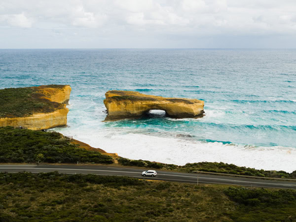 an aerial view of a car passing by the London Bridge, Great Ocean Road