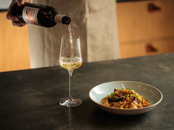 pouring a drink into a glass alongside a dish on the table at Osteria Oggi
