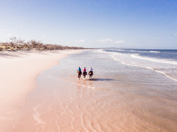 an aerial view of people riding horses along Rainbow Beach