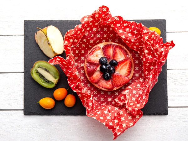 Take away cake inside homemade beeswax wraps. Wrapping food in handmade beeswax wrap cloth indoors, alternative for plastic. Using iron machine to melt beeswax into cotton cloth.