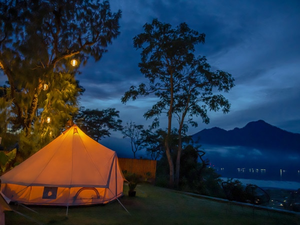 Shot of illuminated tent in a romantic glamping site at night with Mount Batur view.