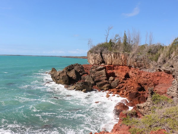 waves lapping against deep ochre rock shelves at Dhimurru Coastal Walking Trail