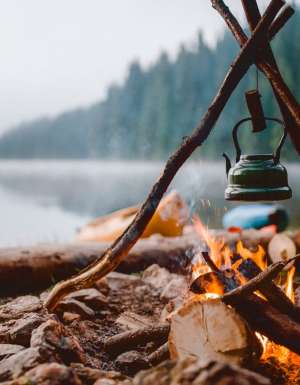 Campfire with a vintage kettle next to the beautiful lake.