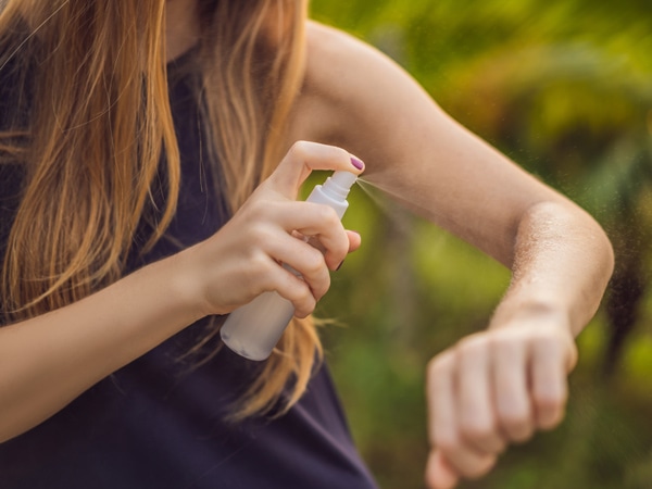 Woman spraying insect repellent on skin outdoor.