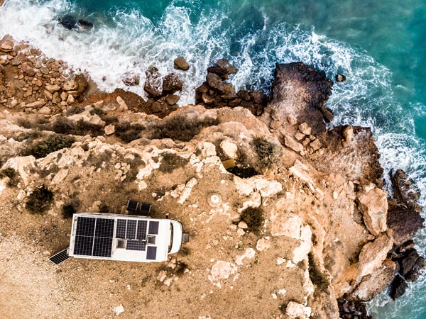 A van with solar panels on the roof camping on cliff sea shore.