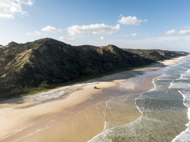 Aerial shot of 4WD driving along the beach at The Cathedrals on k'gari