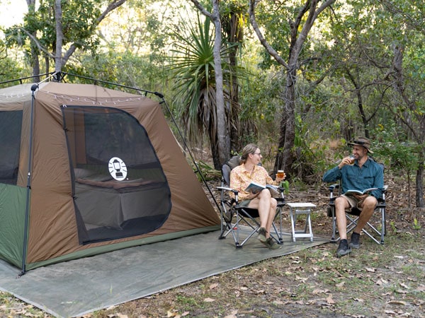 a couple sitting, drinking and reading a book outside their tent in Kakadu