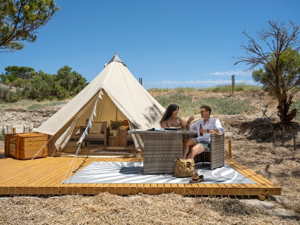 Couple sit at a table in front of glamping tent at Kangaroo Island Seafront Holiday Park.