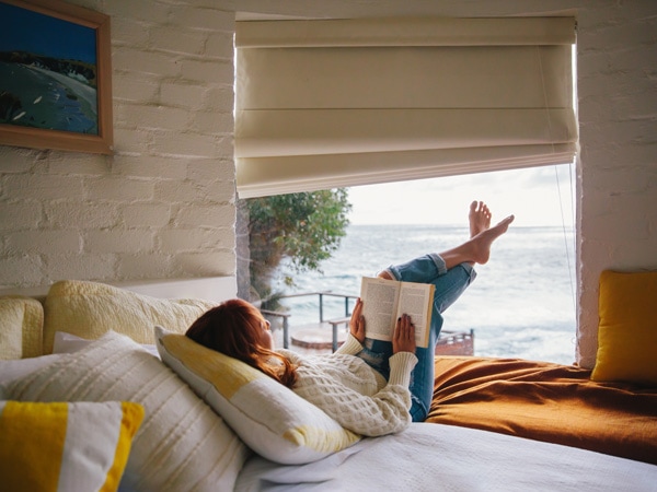 Woman reading book on the bed at The Cliff House on Kangaroo Island. 