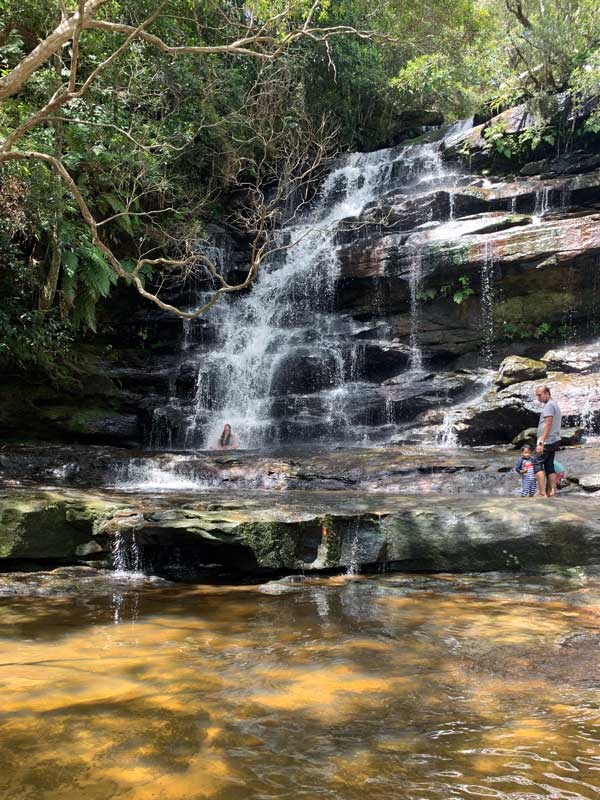 Woman sits under the waterfall at Somersby Falls on the Central Coast