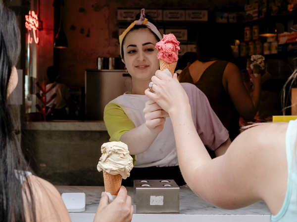 a woman at the counter of a gelato stall handing out ice cream to customers in Pidapipo