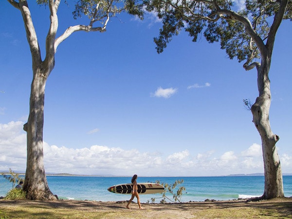 a female surfer holding her surfboard while walking along Noosa National Park