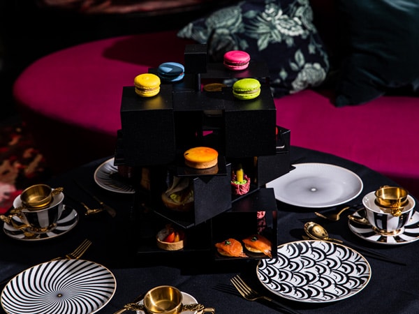 Colourful macaroons, lobster rolls and other high tea goodies sit on a unique black stand with Alice in Wonderland themed decor. (Image: QT Sydney)
