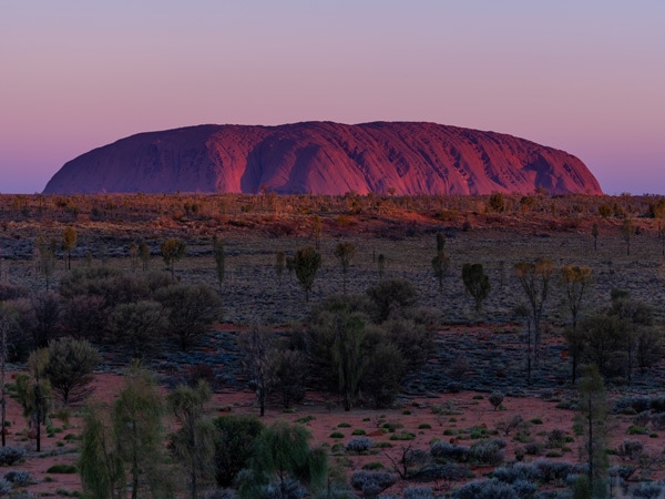 The sun sets over one of the great natural wonders of the world, Uluru towers above the surrounding landscape. (Image: Tourism NT/Che Chorley)
