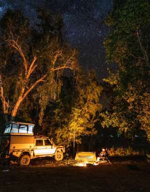 A 4WD is parked by a campfire under the stars at Lorella Springs Wildnerness on the Savannah Way, Northern Territory. (Image: Tourism NT/Sean Scott)