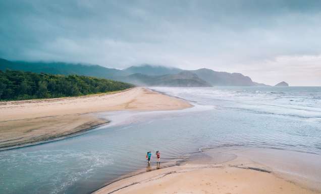 Two people crossing a beach along the Thorsborne Trail