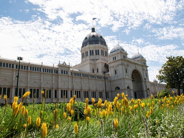 An outdoor view of the Royal Exhibition Building with yellow flowers out the front. (Image: Visit Victoria and Emily Godfrey)