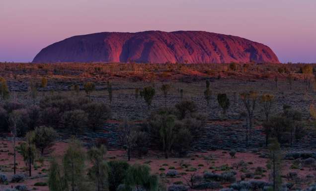 The sun sets over one of the great natural wonders of the world, Uluru towers above the surrounding landscape. (Image: Tourism NT/Che Chorley)