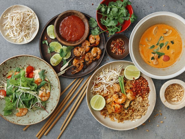 Authentic classic Pad Thai with shrimps. Thai shrimp satay with sweet chili sauce. Tom Yum soup with coconut milk (Tom Khaa). Spicy shrimp salad. Flat lay top-down composition on concrete background.