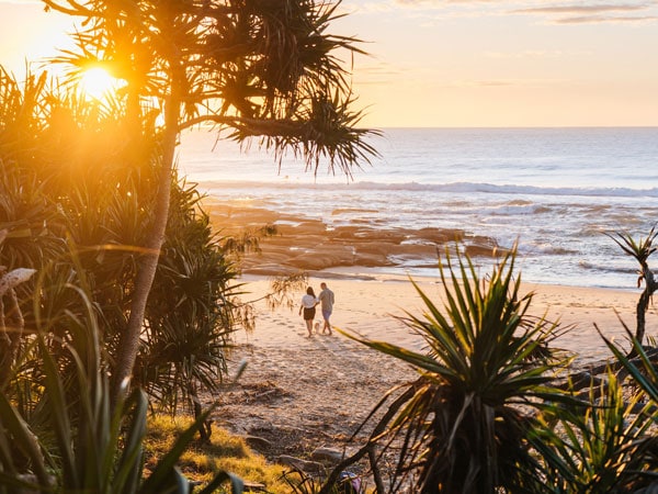 A couple walk along the beach at Point Cartwright. (Image: Visit Sunshine Coast)