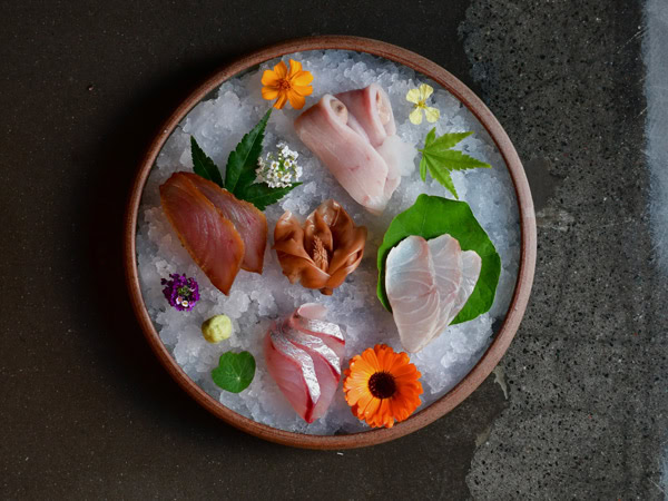 an Ice plate with sashimi, (tuna, silver trevally, swordfish and barramundi) along with wasabi, pickled magnolia and garden flowers at Omotenashi