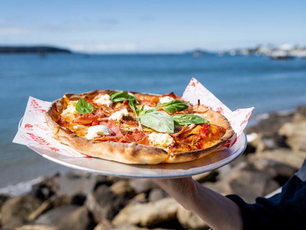 a whole pizza with Batemans Bay in the background at Sam’s Pizza