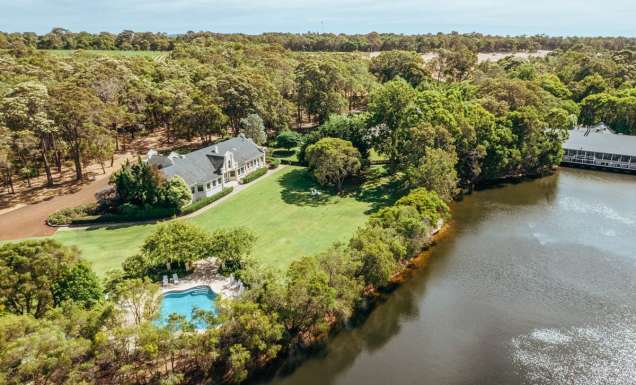 A photo of a white building and a swimming pool surrounded by trees and a river viewed from above.