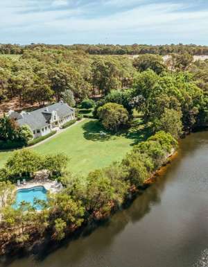 A photo of a white building and a swimming pool surrounded by trees and a river viewed from above.