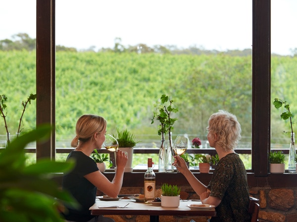Two women sitting at a table indoors with a wine glass in their hand and looking out the window.
