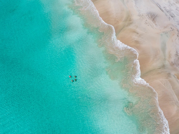 Aerial shot of people swimming in Emu Bay's turquoise waters. 