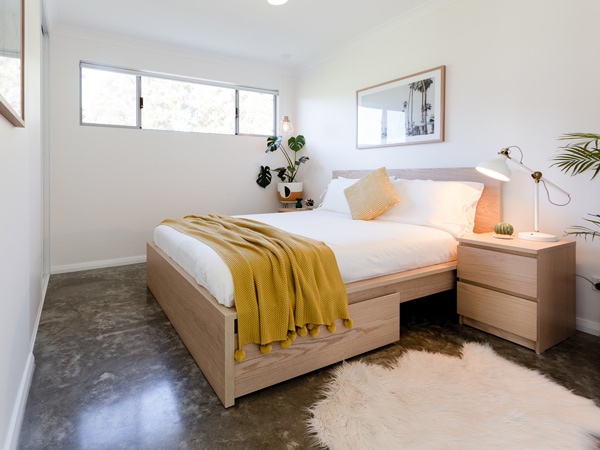 A photo of a bedroom indoor with a bed, bedside table and frames on the wall.