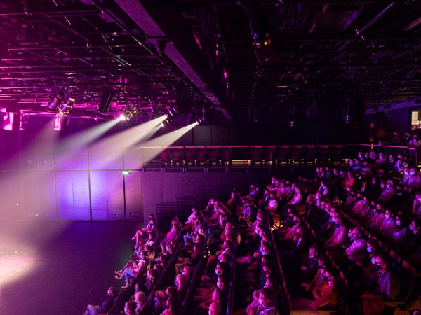 A photo of a theatre in the dark with people sitting and watching the scene.