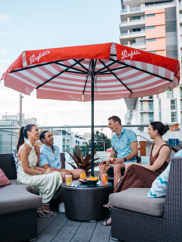 friends enjoying drinks under a huge red umbrella at Soleil Pool Bar at Rydges South Bank Brisbane