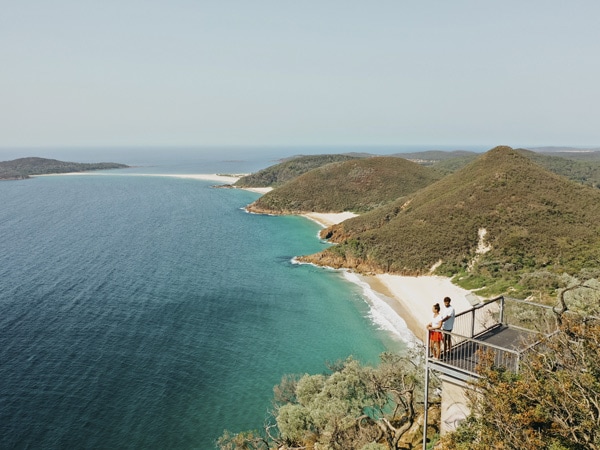 Two people standing on a platform overlooking the ocean and mountains.