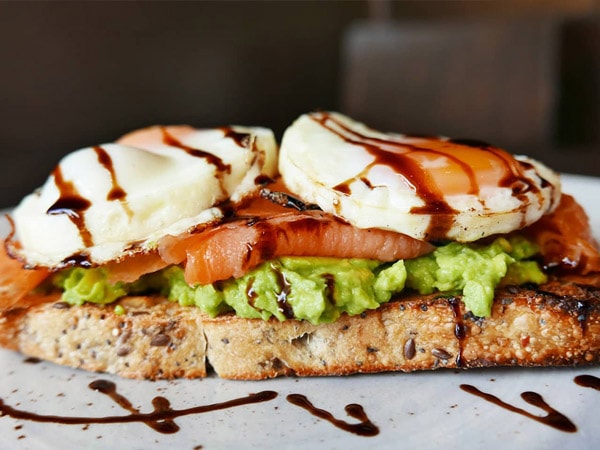 Bread on a white plate with avocado, eggs and salmon