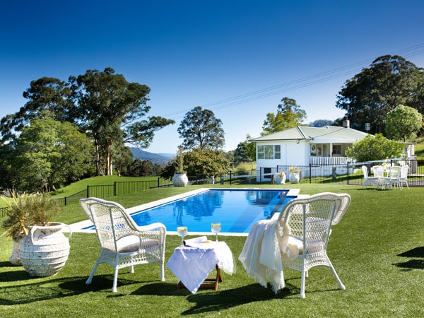 Two chairs sit beside a pool on lush green grass at a rustic farmhouse in Australia