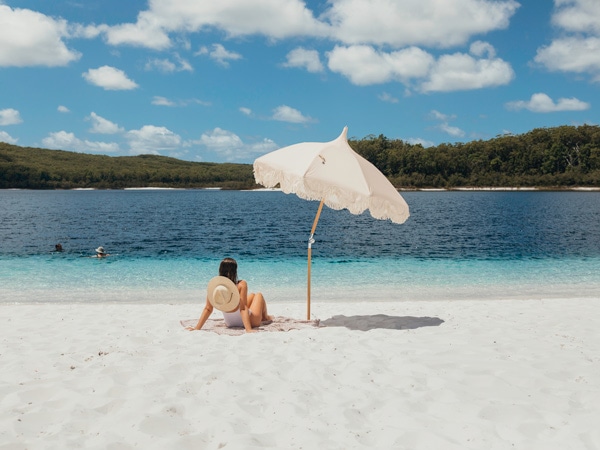 Woman sitting under umbrella on sand at Lake McKenzie.
