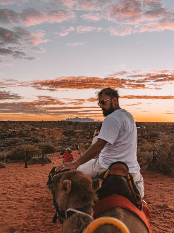 a man riding a camel before sunset in Uluru