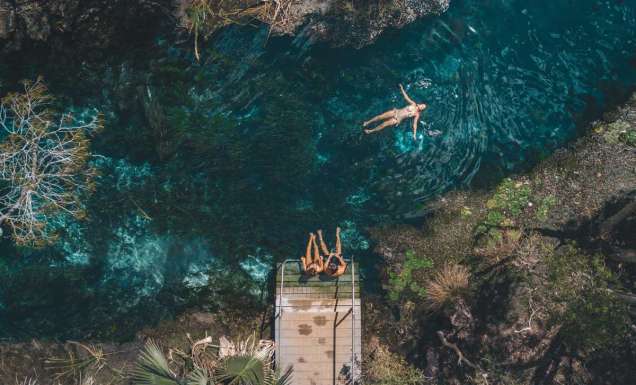 an aerial shot of a girl floating and two girls sitting on the edge of Mataranka Thermal Pool