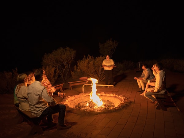 a group of people sitting around a bonfire during their Tali Wiru dining experience