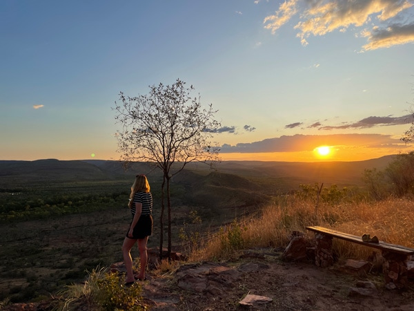 a woman gazing at the sunset on top of a hill