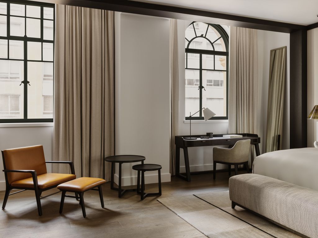 A stylish hotel room blending heritage charm and modern design, featuring steel-framed windows, minimalist furniture, and contemporary decor.
