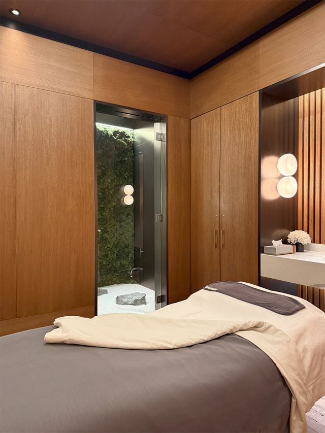 Spa treatment room with a massage bed, featuring timber walls and a serene Japanese-style garden visible through a window.