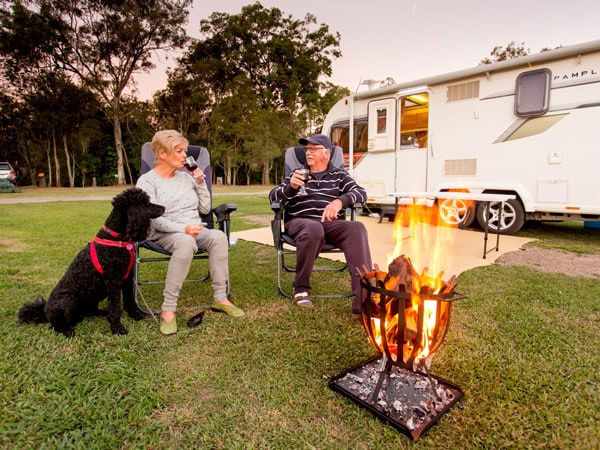 an old couple sitting by a bonfire with their dog outside their campervan at Big4 Gold Coast Holiday Park