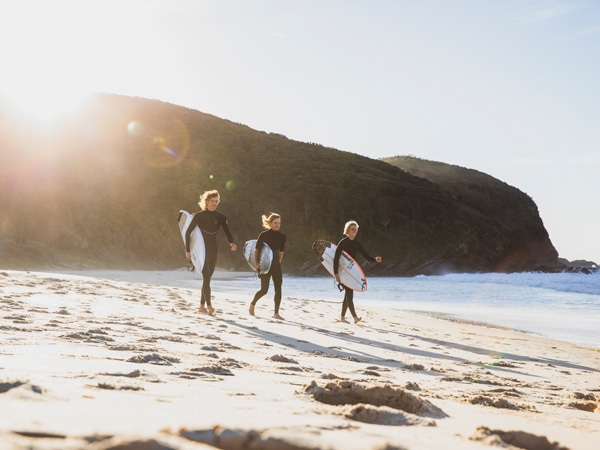 three surfers heading out into the water at Elizabeth Beach in Booti Booti National Park