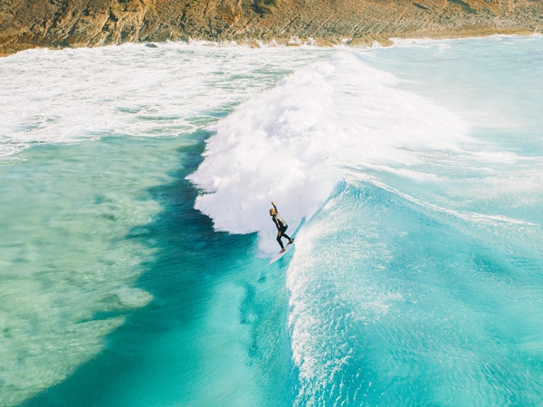 an aerial view of a person surfing on the turquoise blue waters, Hola Palms, Boomerang Beach