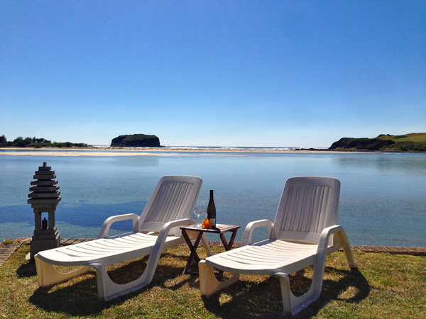 two sun loungers by the river with a wine bottle on the table at Minnamurra Beach House