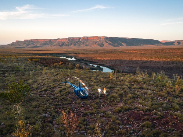 a couple stands on a cliff edge marvelling at the vast landscapes and towering escarpments on a helicopter tour at El Questro Station