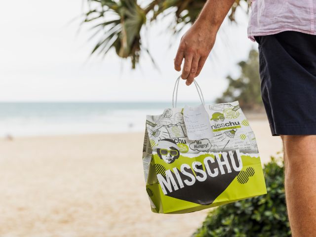 a person holding a Misschu Noosa paperbag at the beach